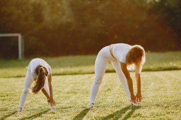 Two girls stretching on a sunny day in a green field, preparing for exercise.